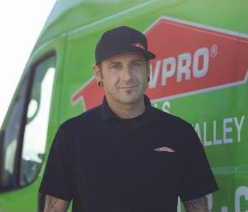 Man in black hat and black shirt in front of green SERVPRO van